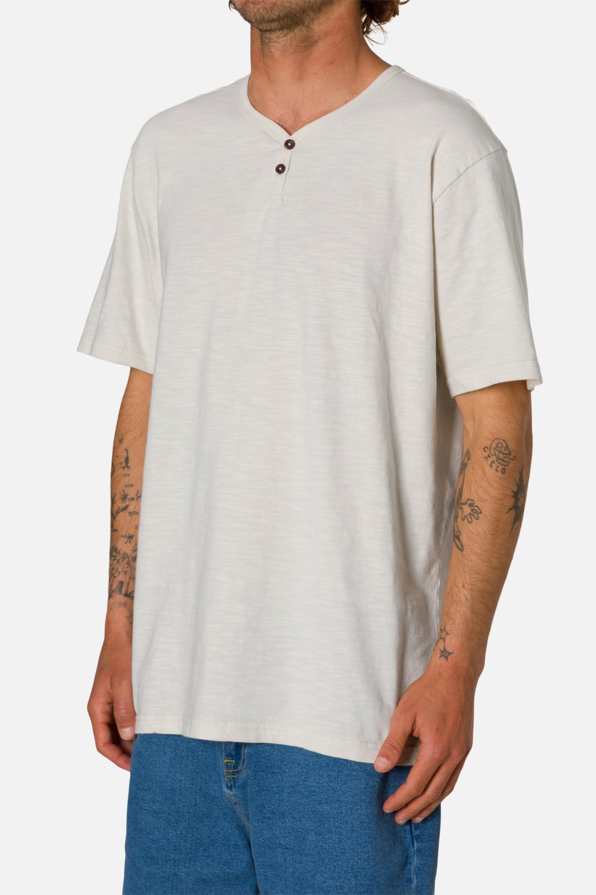 Man wearing a white henley shirt and blue jeans on a white background