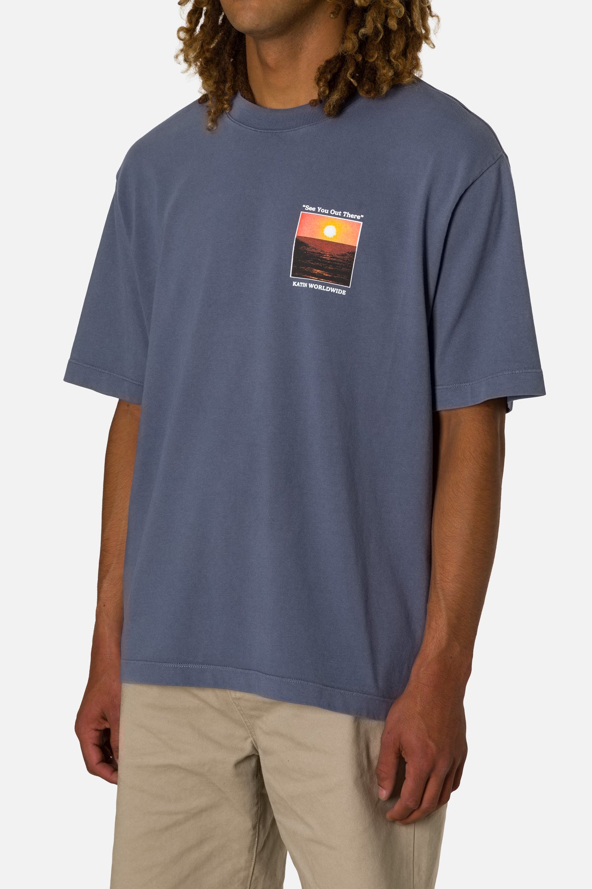 Person wearing a blue t-shirt with a sunset graphic on a plain background