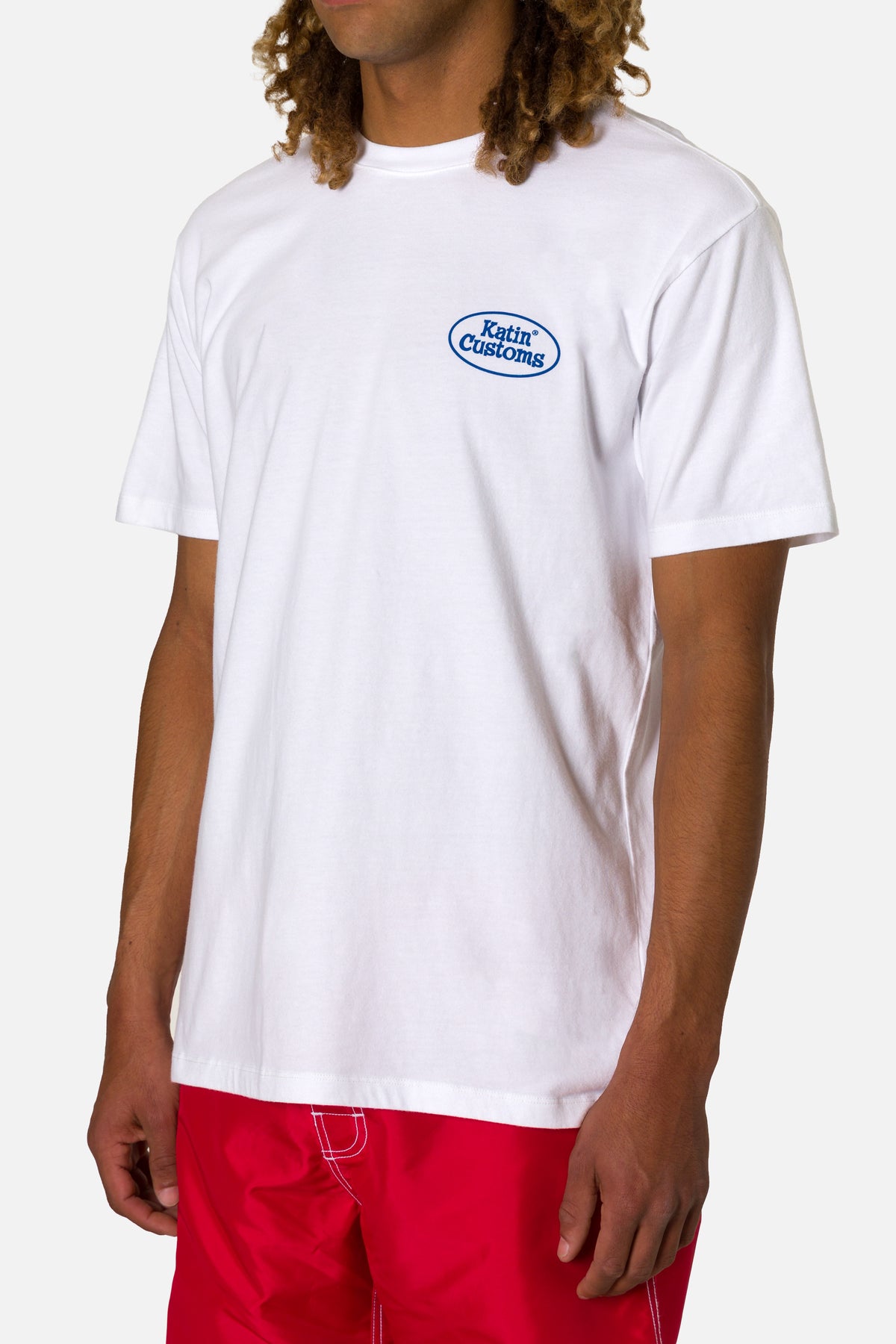 Person wearing a white t-shirt with a logo and red shorts on a white background