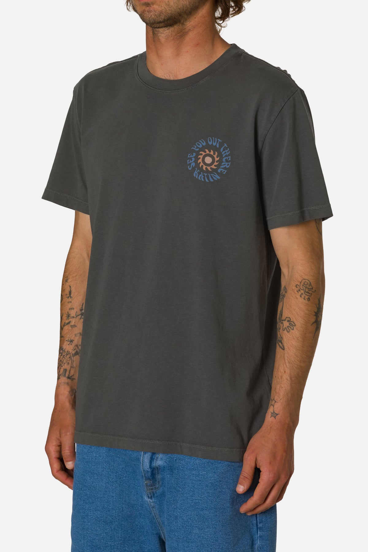 Person wearing a dark gray t-shirt with a small see you out there graphic on a white background