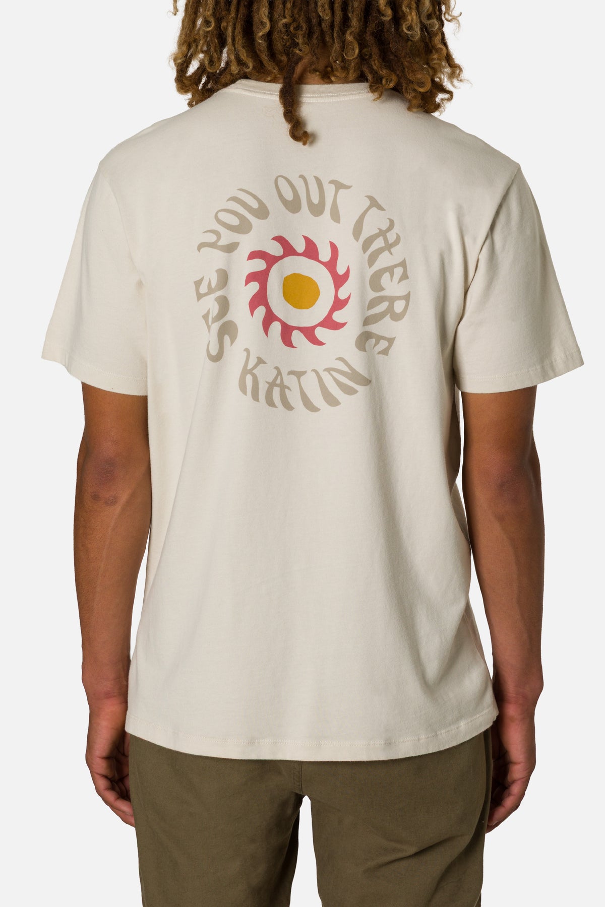 Person wearing a beige t-shirt with a graphic design on the back, standing against a white background.