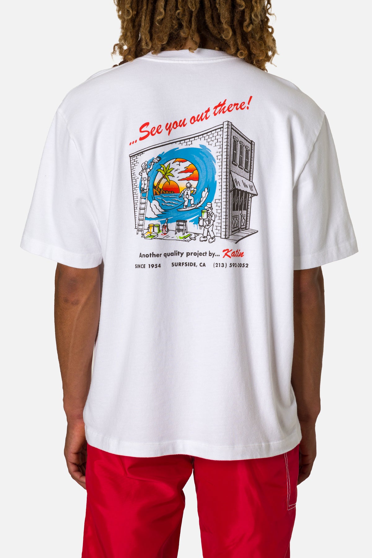 Person wearing a white t-shirt with a colorful graphic and text on the back, standing against a plain background.