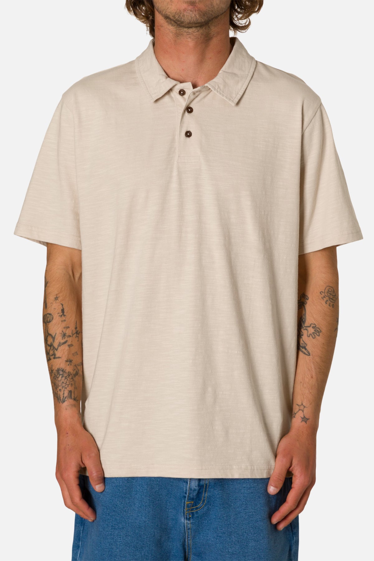 Man wearing a beige polo shirt and blue jeans on a white background