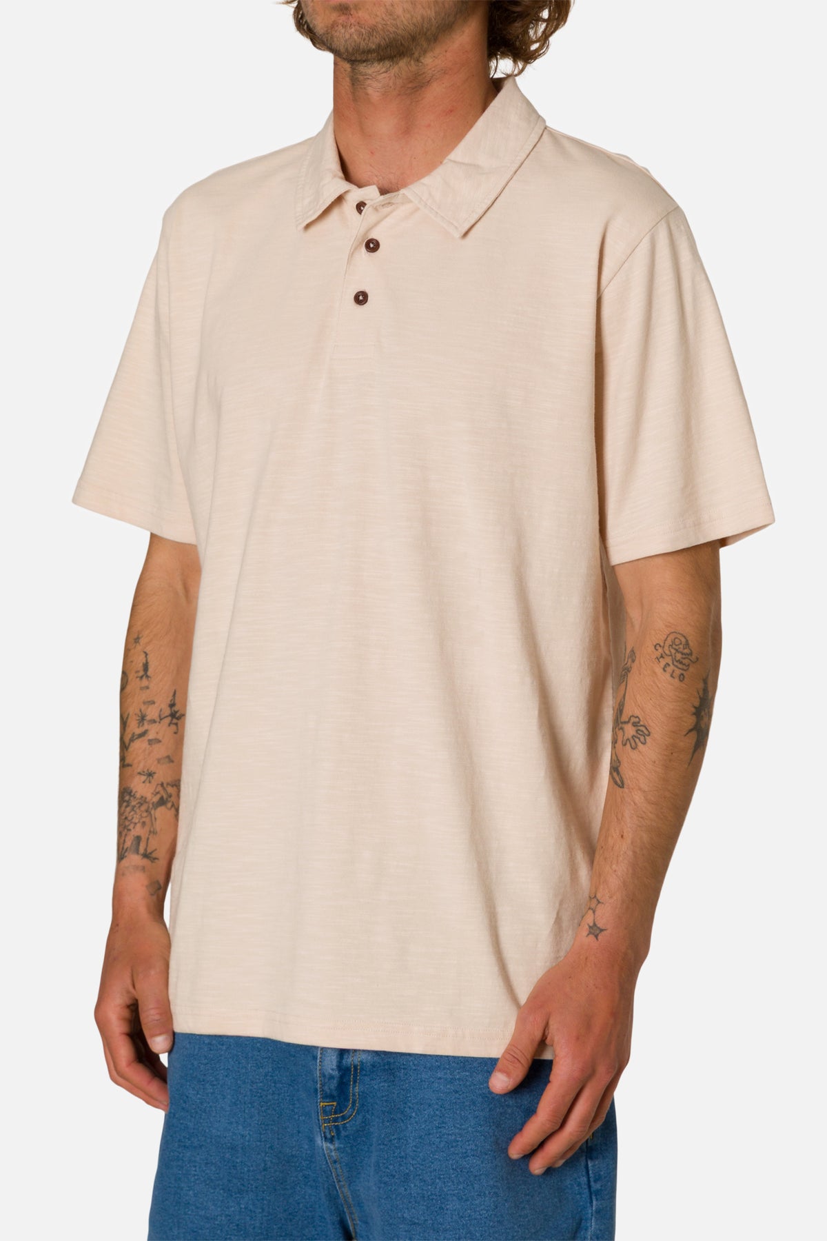 Man wearing a beige polo shirt and blue jeans on a white background