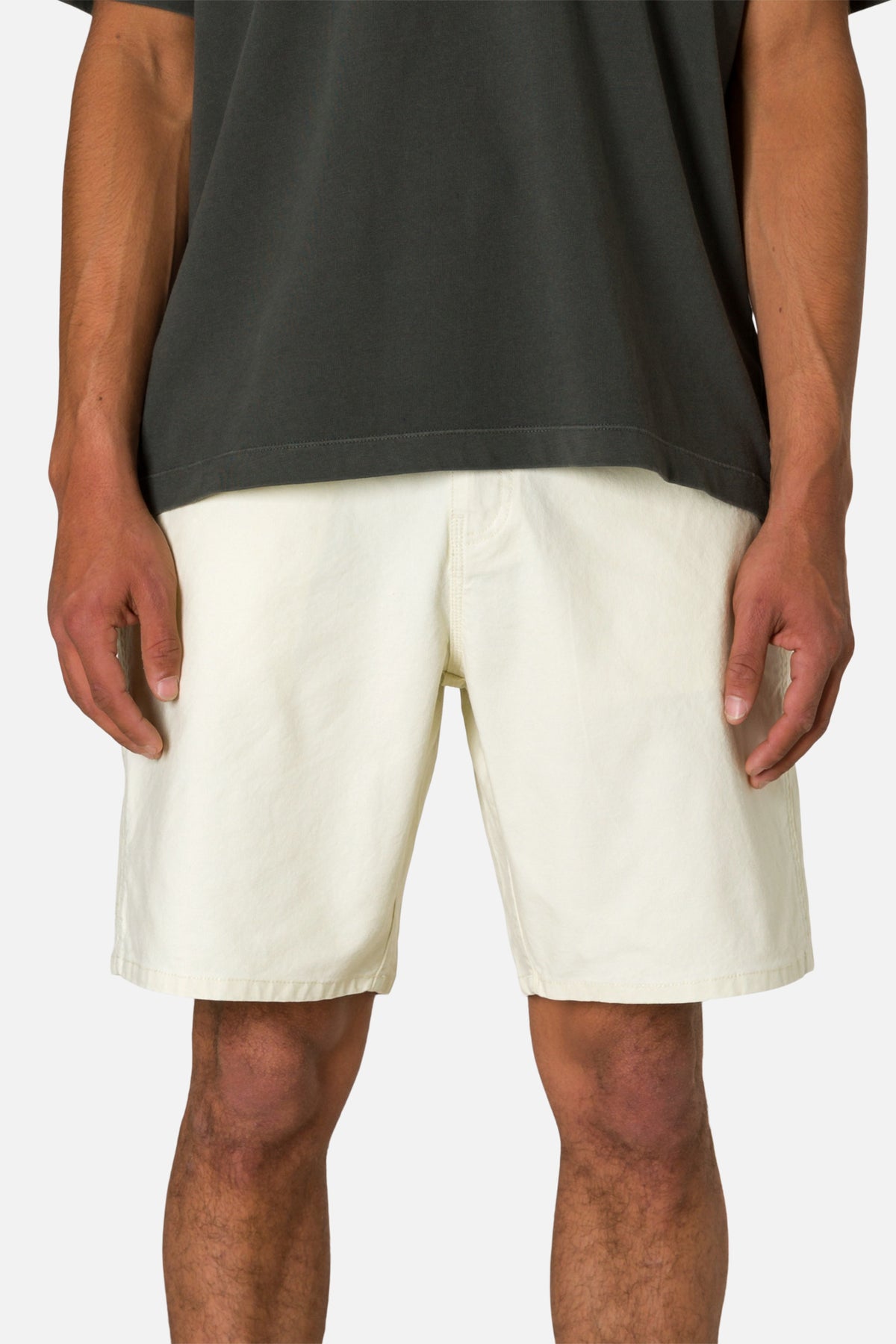 Front view person wearing off white shorts and a black shirt on a plain background