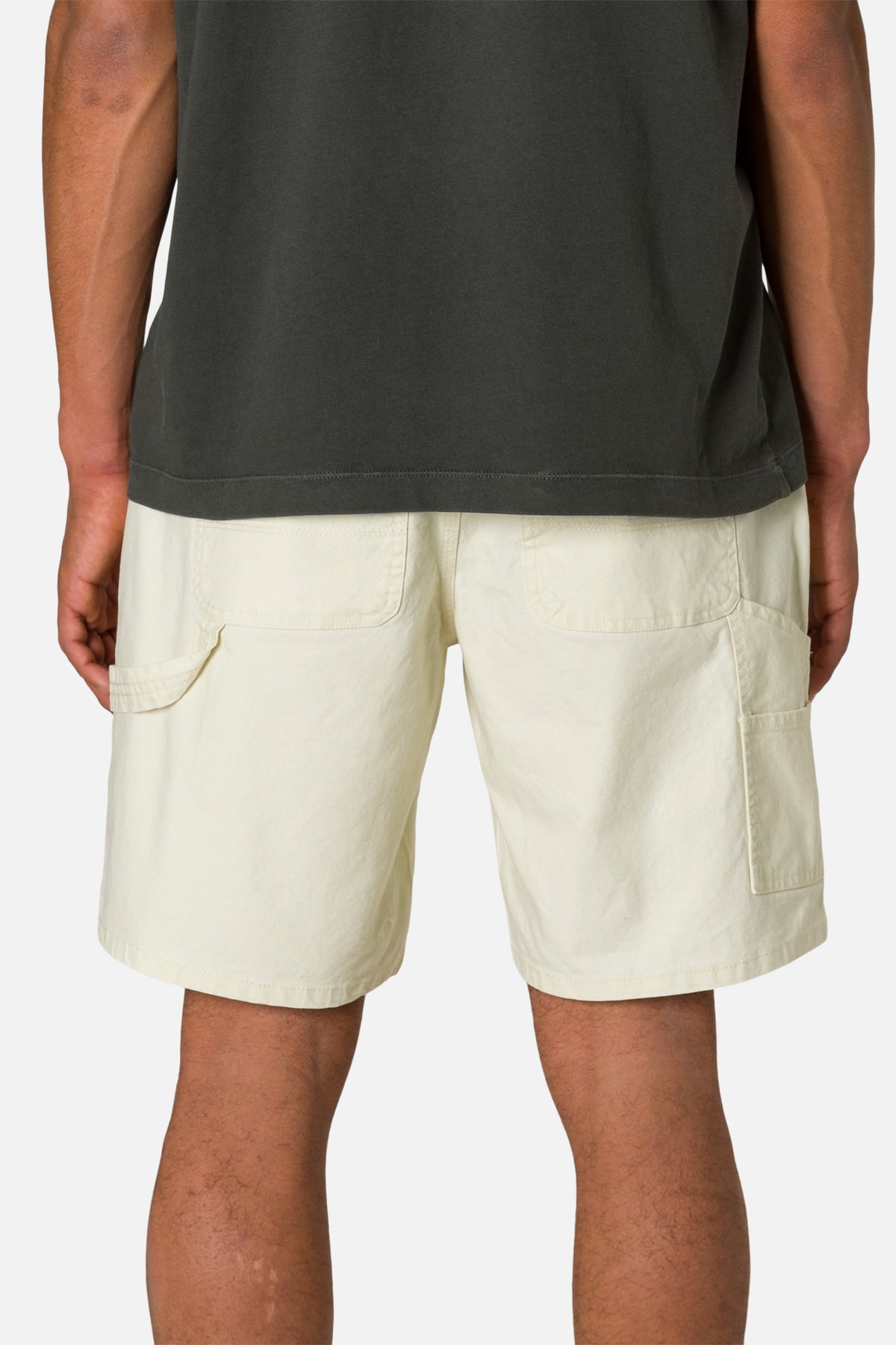 Back view person wearing off white shorts and a black shirt on a plain background