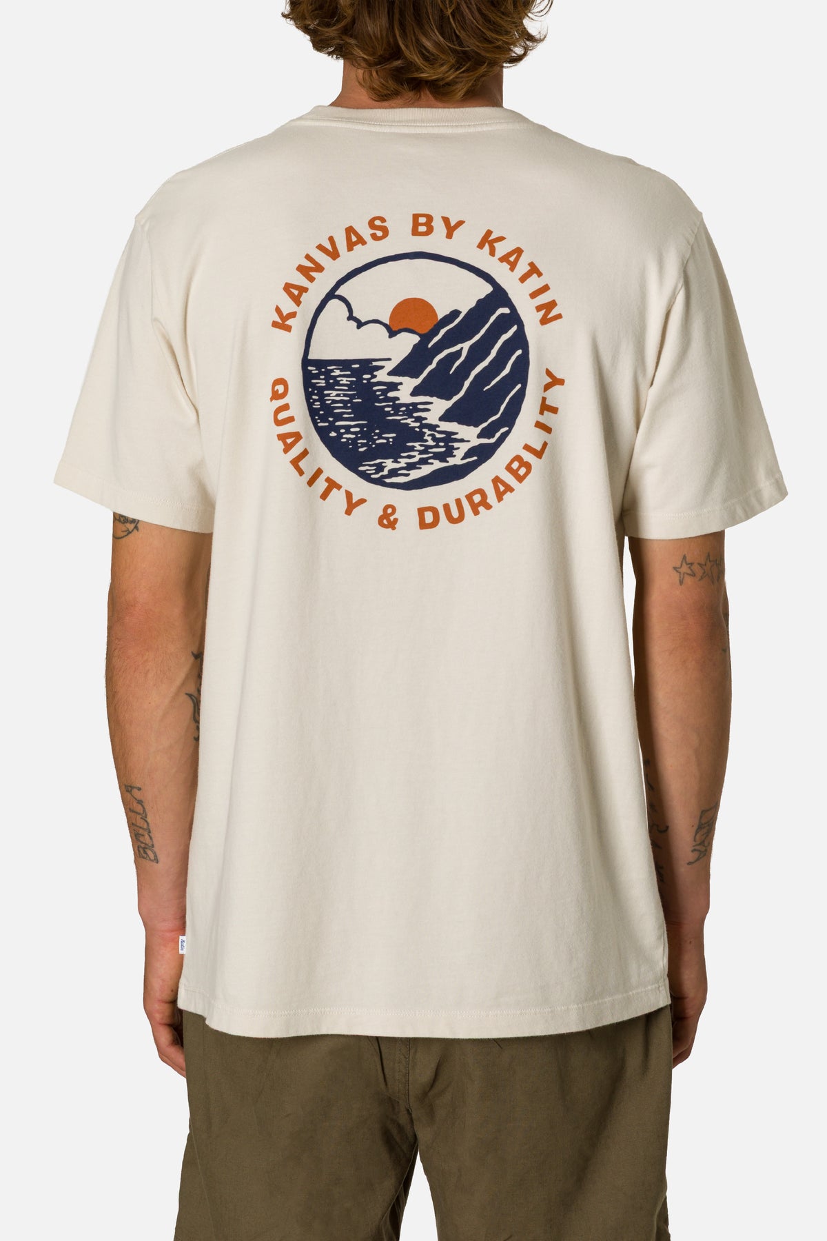 Person wearing a beige t-shirt with a graphic design on the back, standing against a white background.