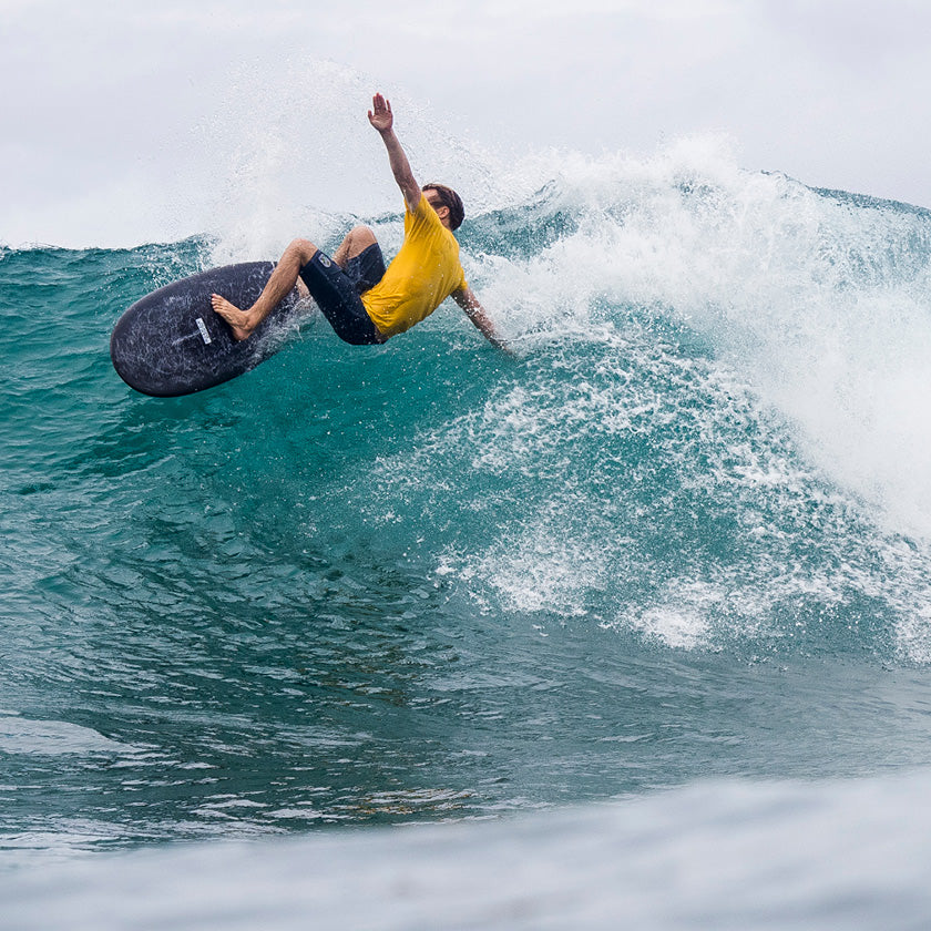 Surfer in a yellow T-shirt and dark boardshorts carving a turquoise wave.