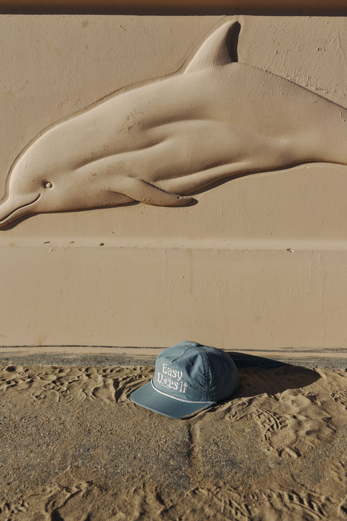 Sand sculpture of a dolphin on a sandy surface with a cap in the foreground.