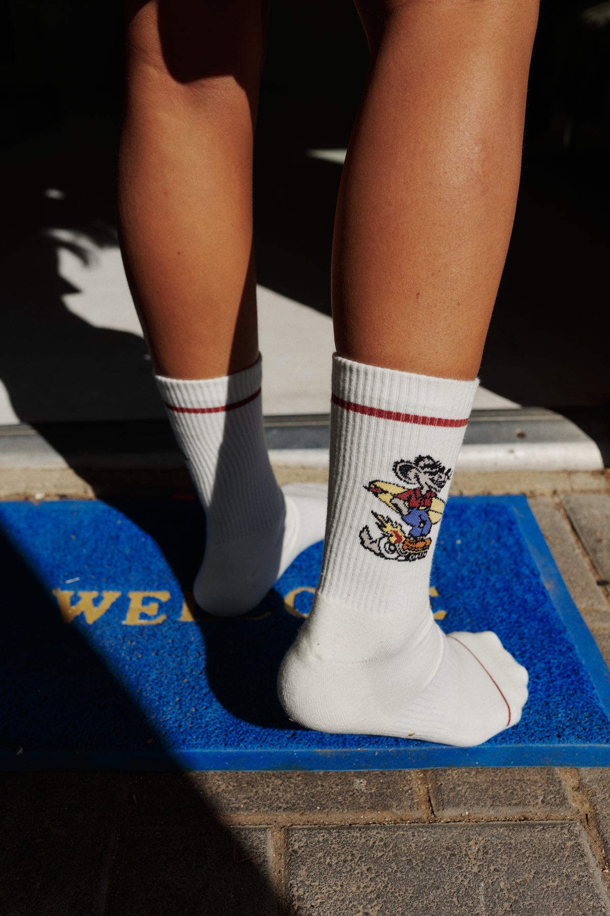 Person wearing white socks with a cartoon character design on a blue doormat.