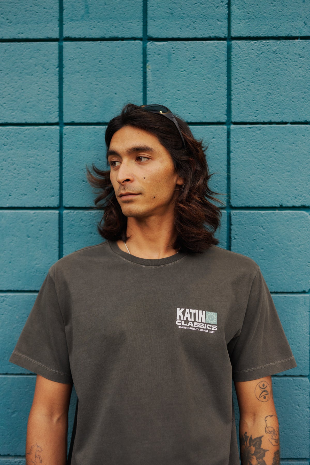 Person wearing a dark gray t-shirt with a logo against a blue tiled wall