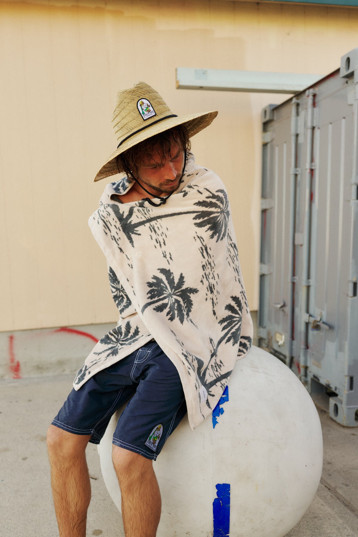 Person sitting on a large white ball wearing a patterned towel and straw hat.