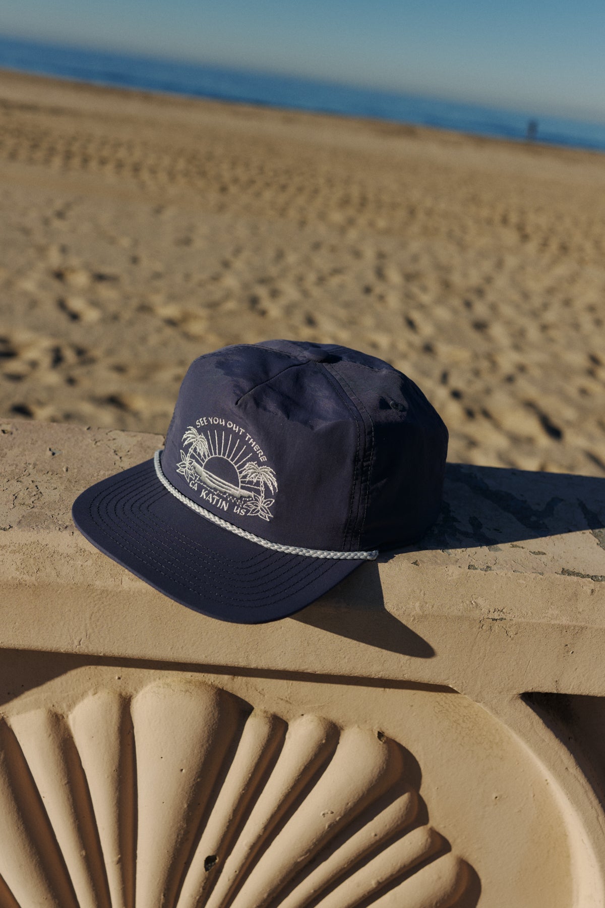 Navy blue cap with white logo on a sand sculpture at the beach