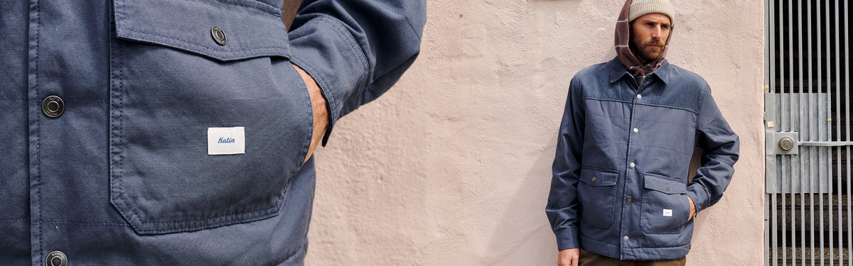 Close-up of the Yukon Jacket in Washed Blue showing its snap flap pocket and Katin label, beside a man wearing the jacket with a corduroy collar and yoke against a pink stucco wall