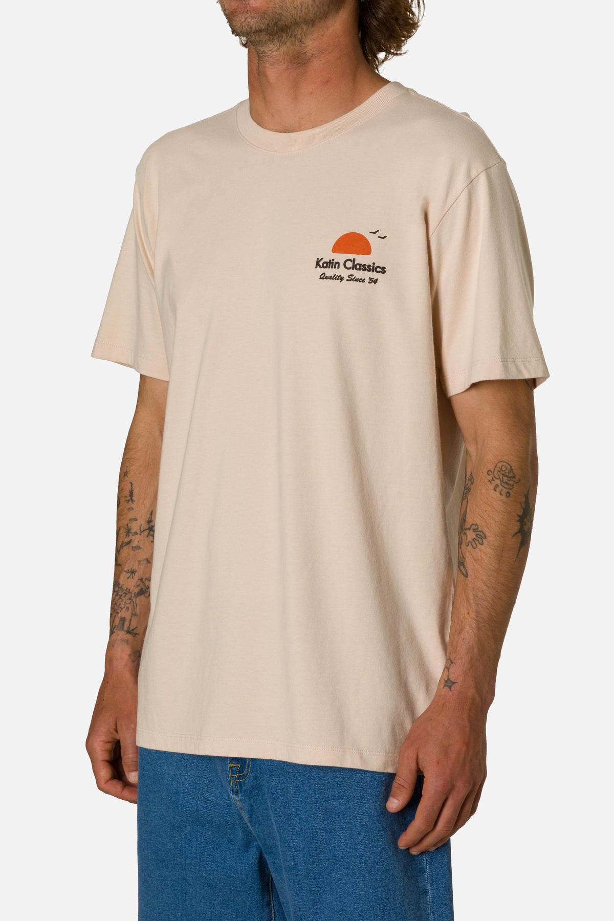 Person wearing a beige t-shirt with a logo on a plain background