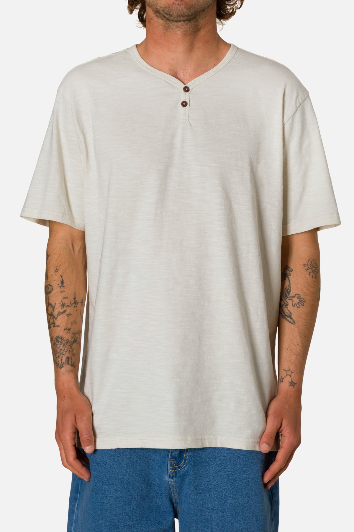 Man wearing a white henley shirt and blue jeans on a white background