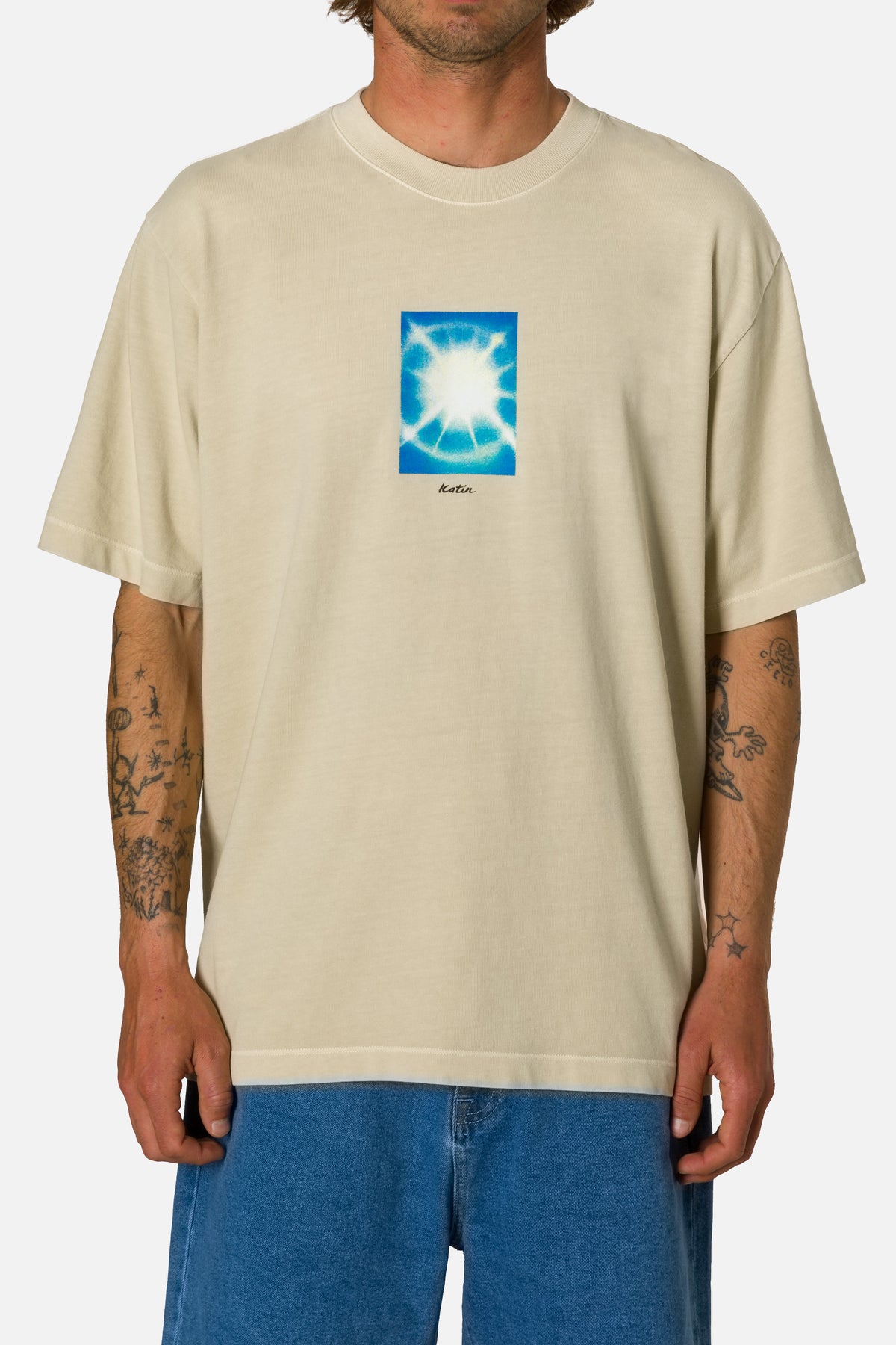 Person wearing a beige t-shirt with a blue graphic design on a white background