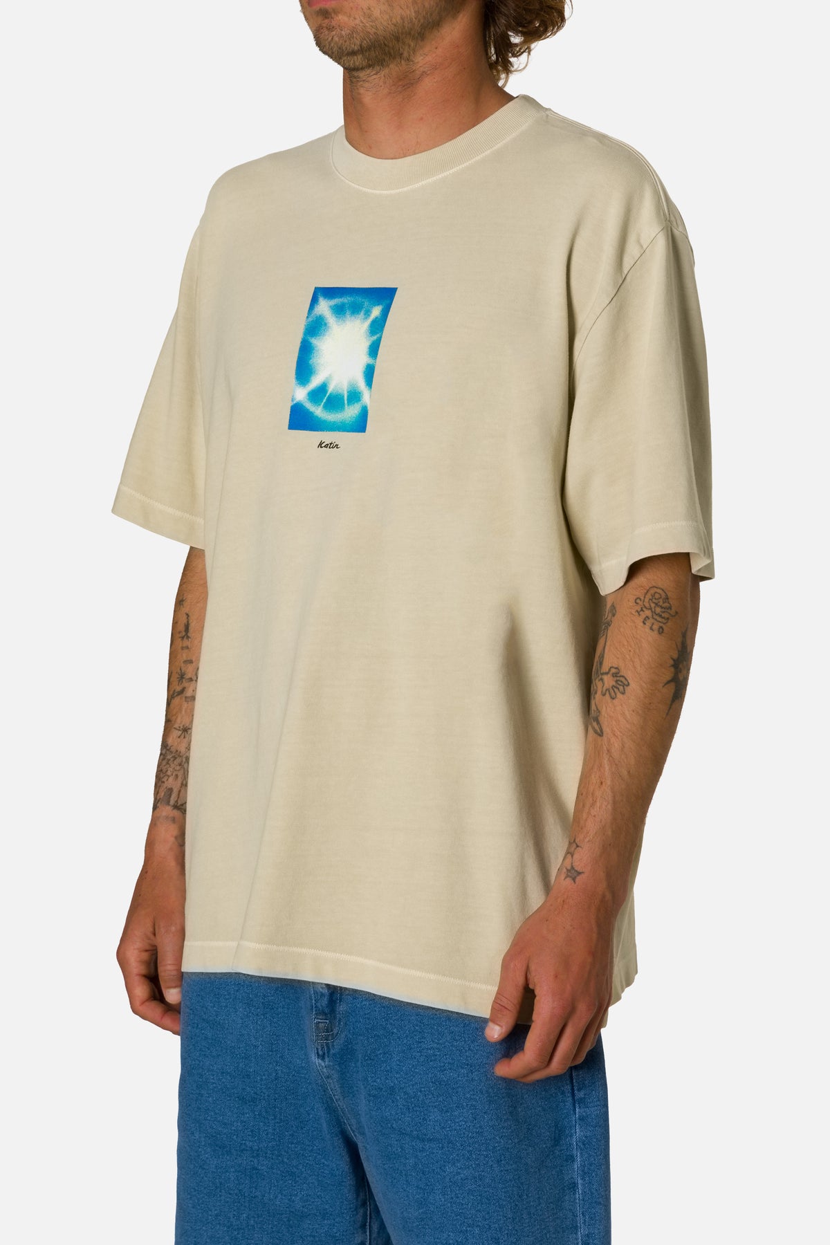 Man wearing a beige t-shirt with a graphic design on a white background