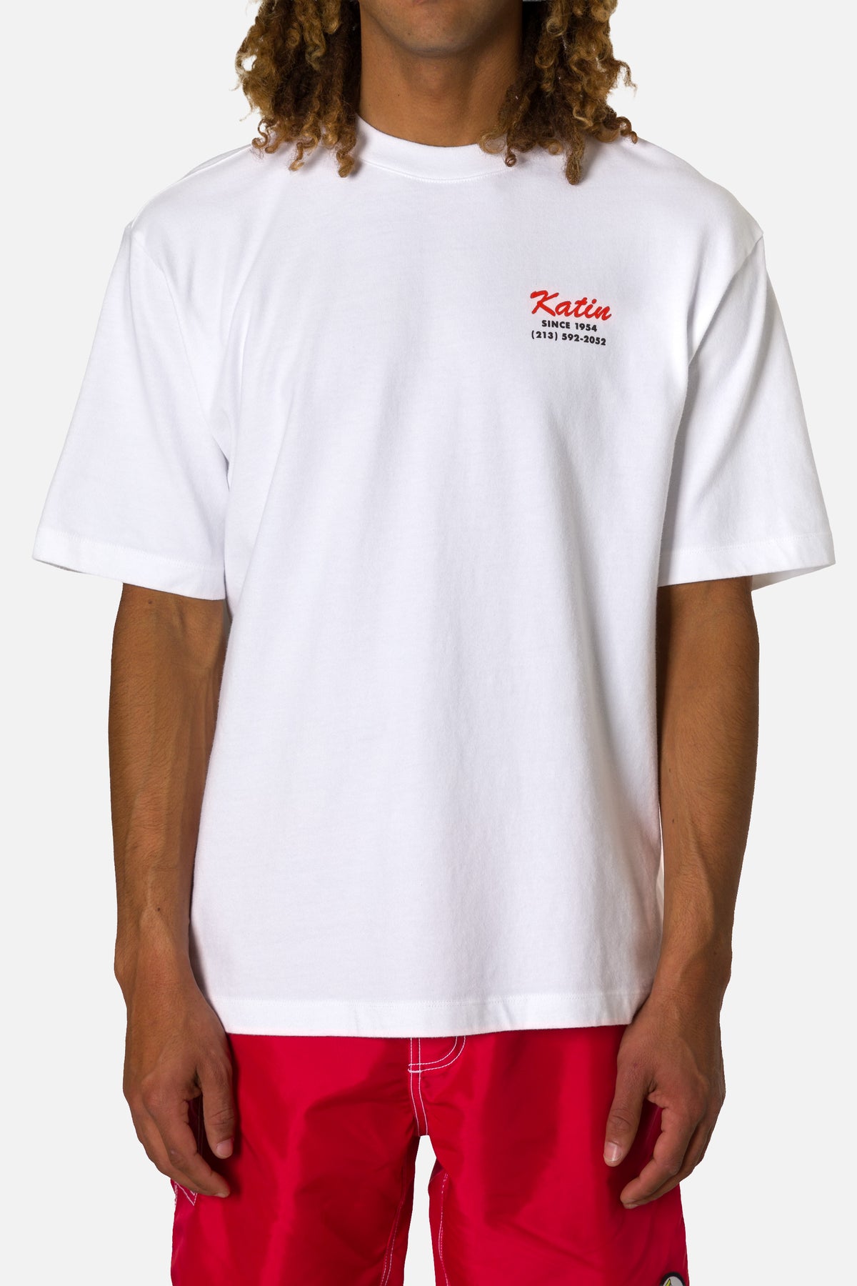 Person wearing a white t-shirt with a logo and red pants on a white background