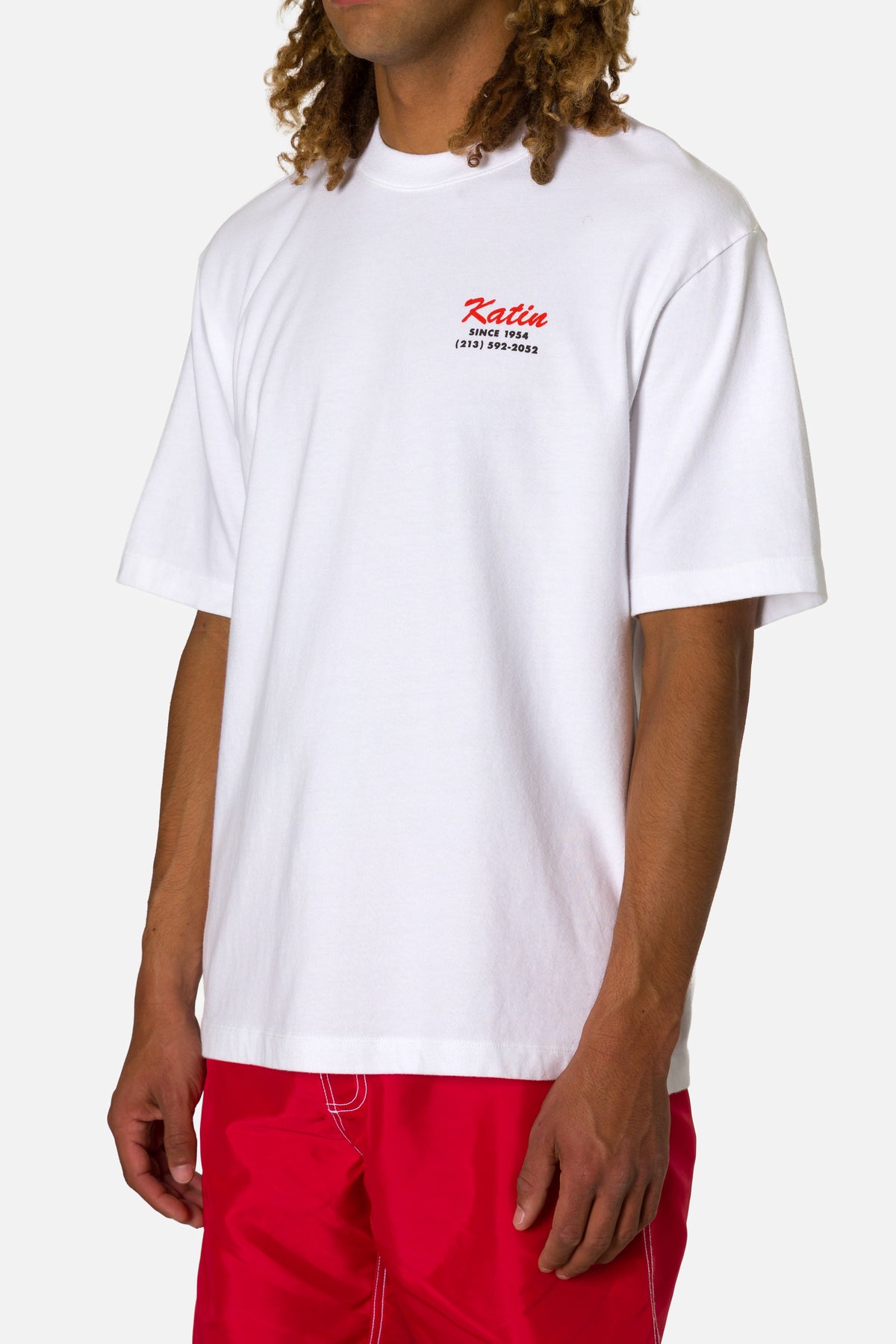 Person wearing a white t-shirt with a logo and red shorts on a white background