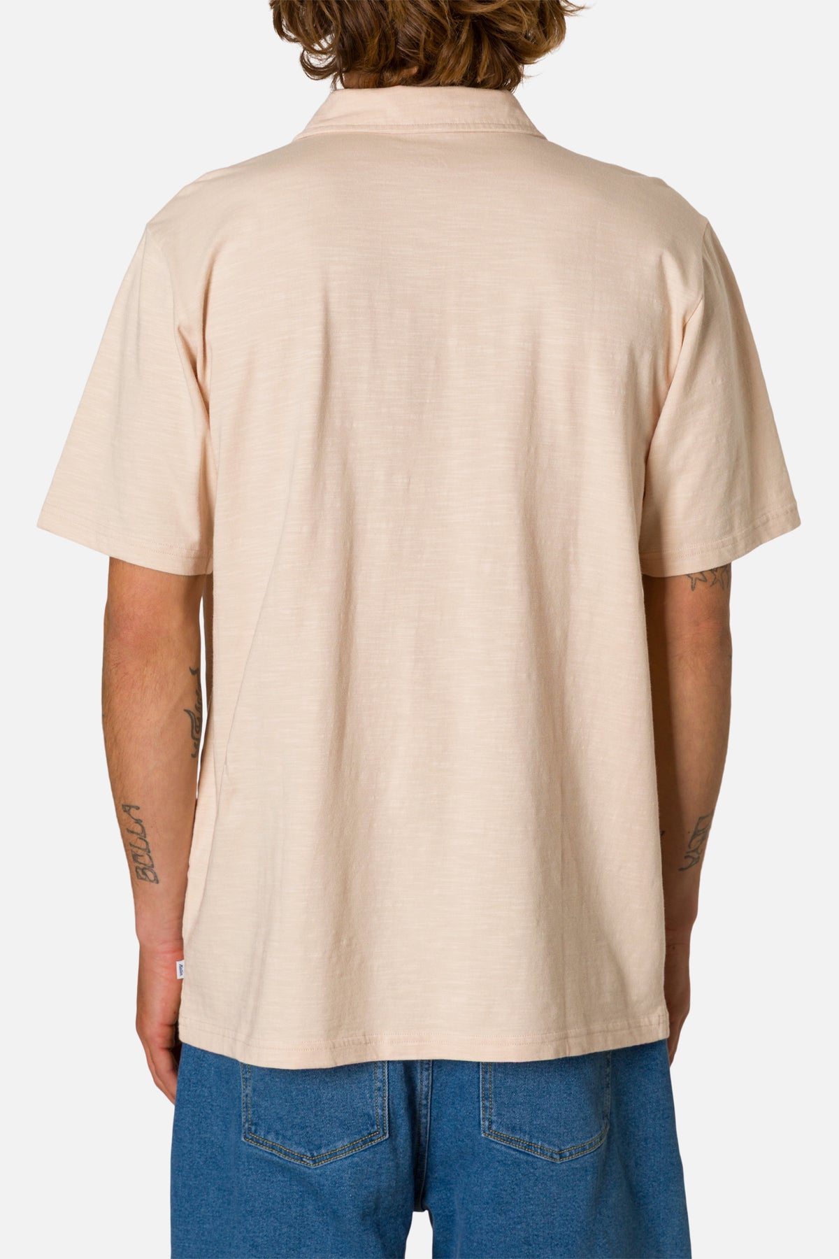 Person wearing a beige polo shirt and blue jeans on a white background