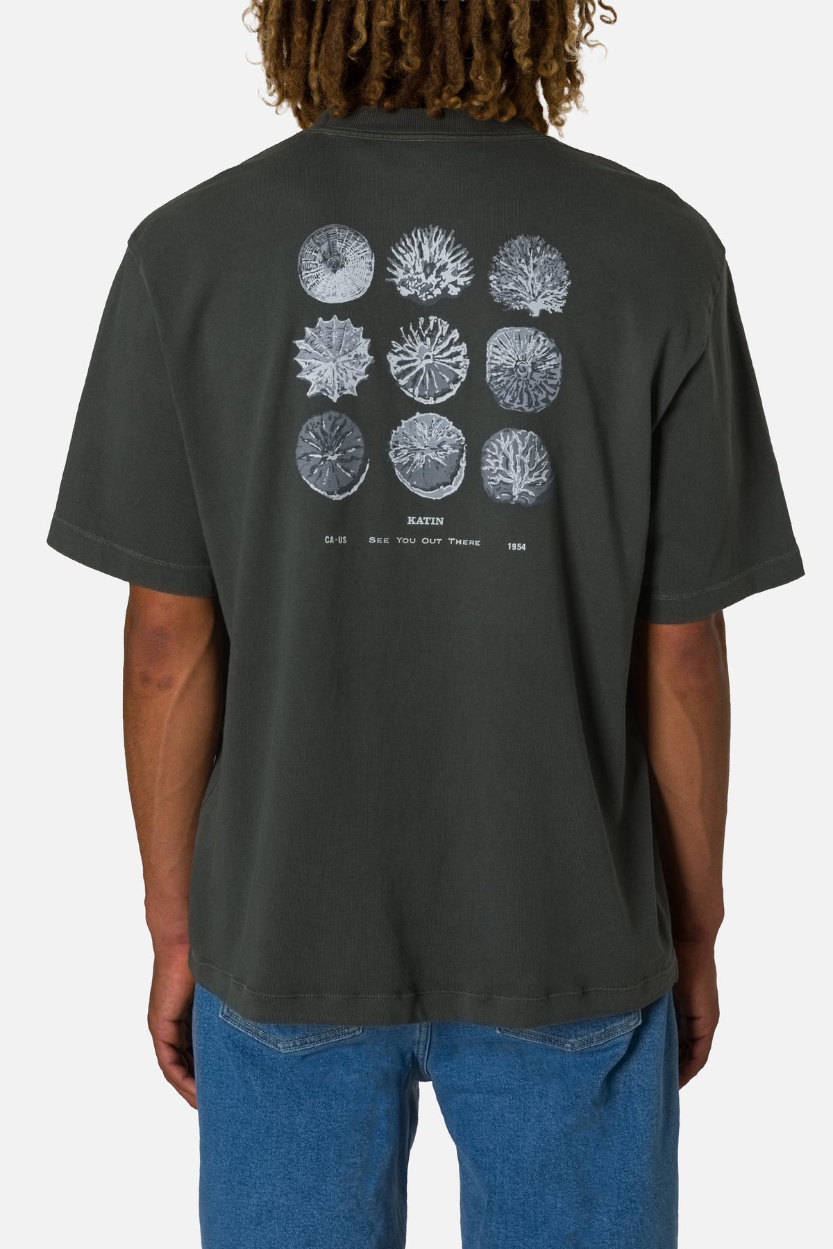 Person wearing a black t-shirt with coral reef design on the back, standing against a white background