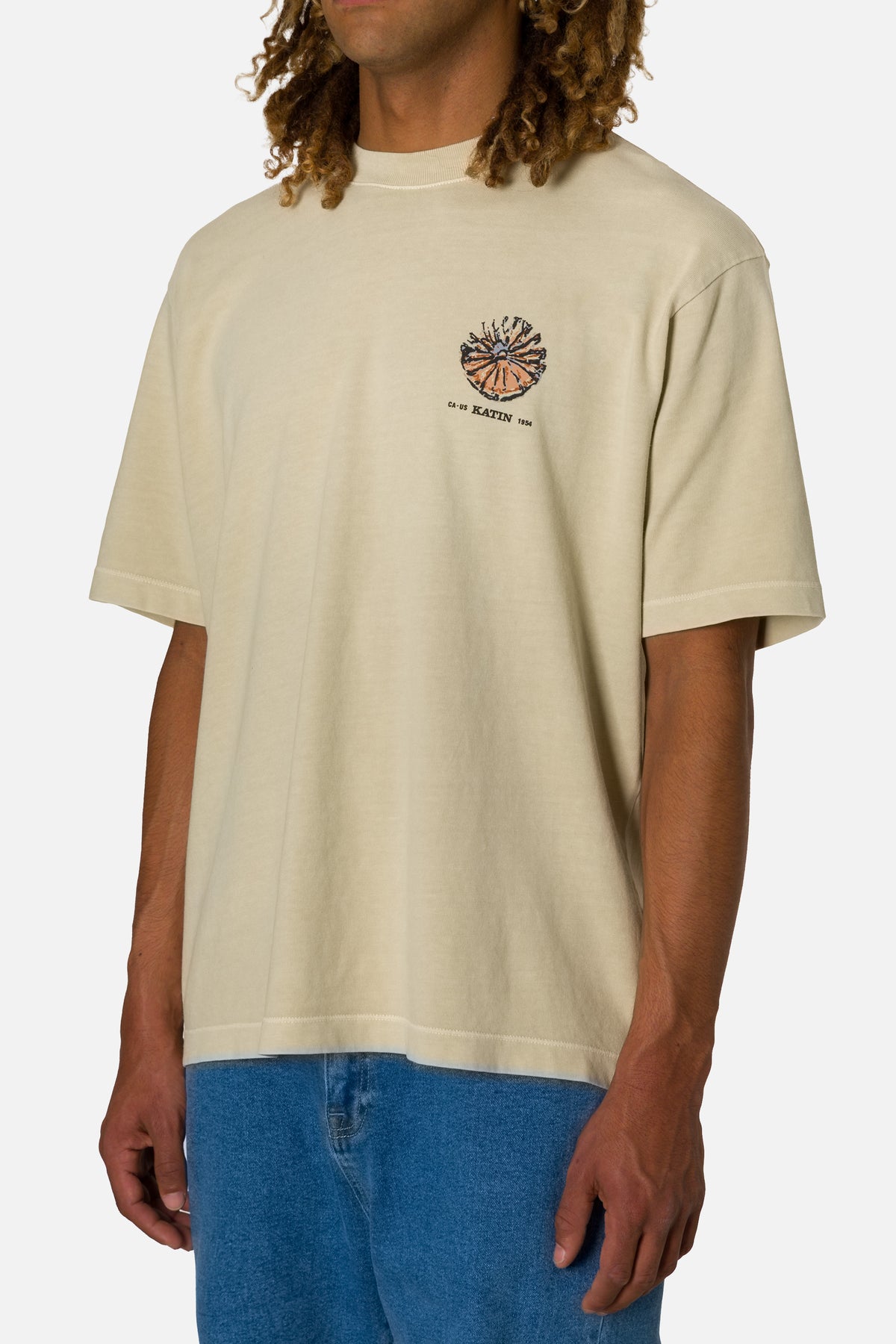 Person wearing a beige t-shirt with a logo on a plain background