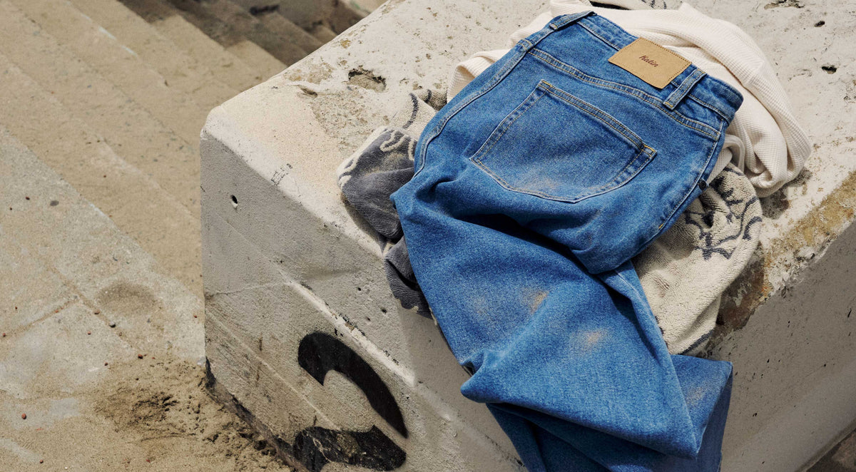 Denim jeans laying on a sandy wall with sand on them and Katin leather patch on wiastline above pocket