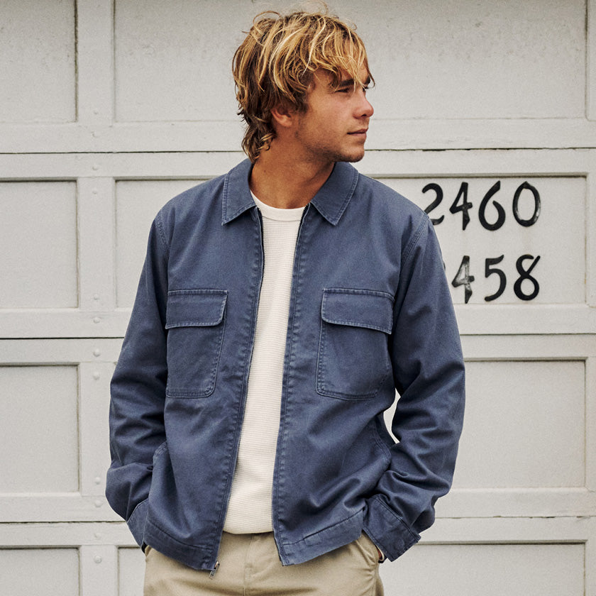 Man in a blue zip-front jacket over a white shirt standing against a white garage door.