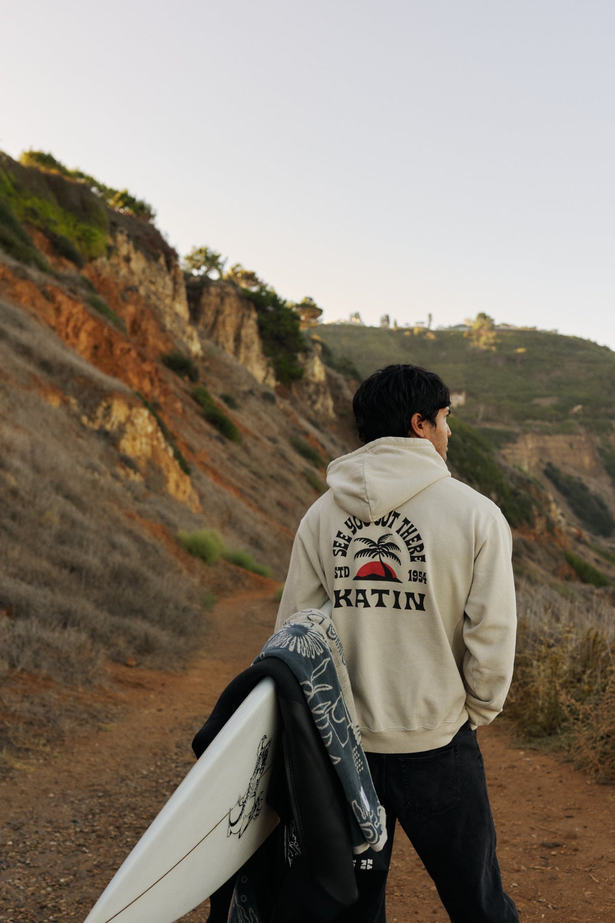 Person holding a surfboard with a scenic view of a coastal landscape.