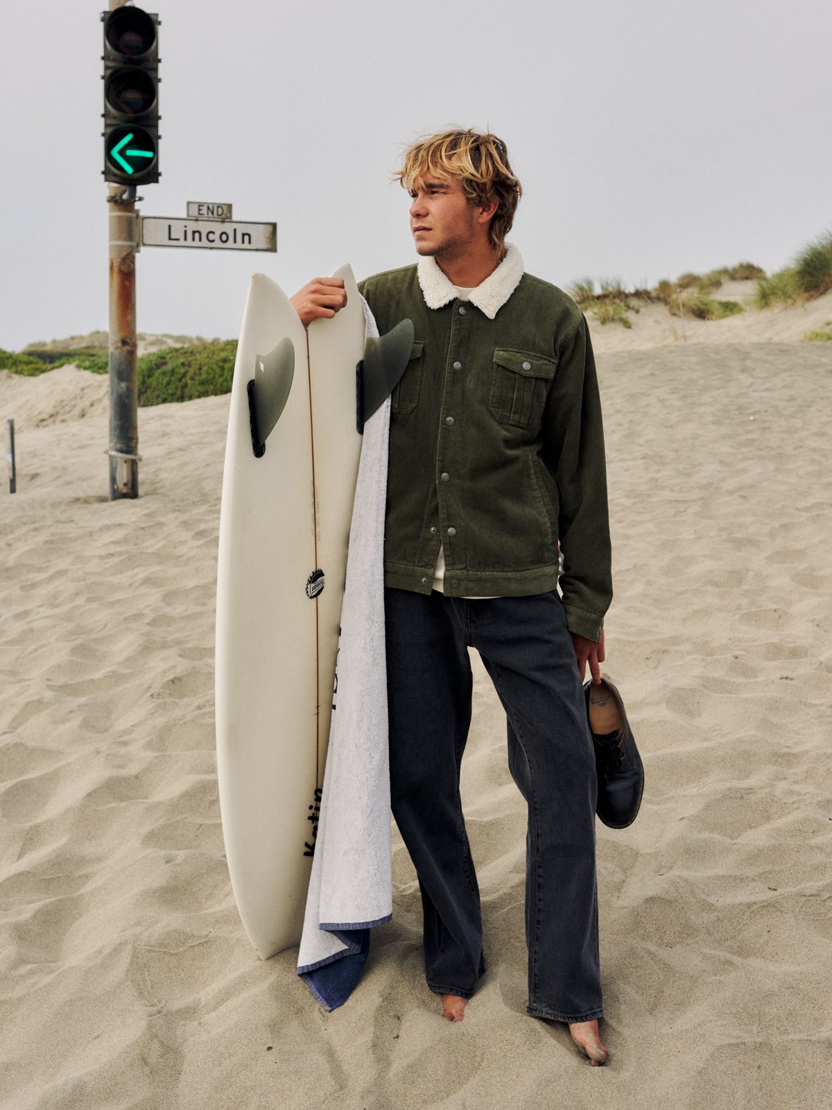 Katin Harris Corduroy Jacket in Dark Olive, 8-wale cotton corduroy with sherpa collar, on model with a surfboard on the beach, lifestyle #color_dark olive