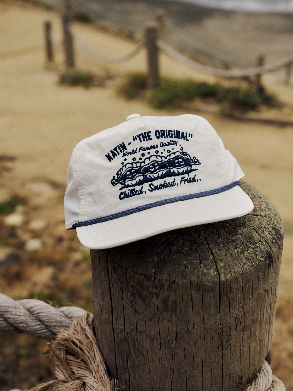 Katin Shuck Hat in Vintage White, recycled nylon five-panel with rope and “The Original” oyster embroidery, on a wooden post, lifestyle #color_vintage white